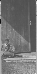 SA0142 - Unidentified man sitting in the front of a large door to a building.